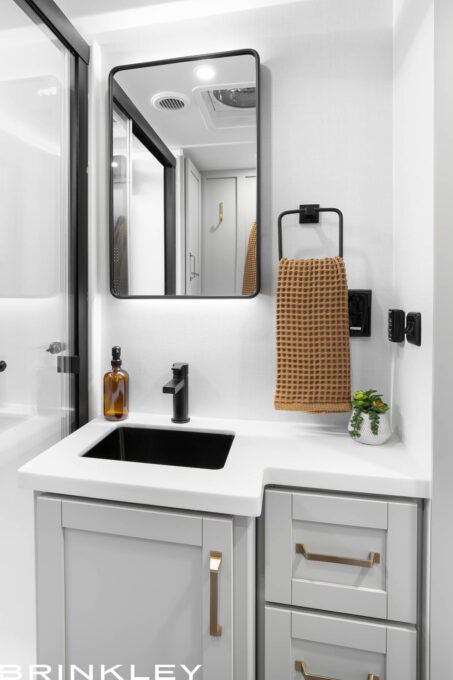 Close-up view of a luxury Brinkley RV Model Z Fifth Wheel bathroom vanity featuring premium cabinetry and a backlit recessed medicine cabinet.