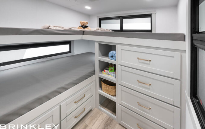 2026 Brinkley Model Z 2810 Fifth Wheel Rear Bunkhouse Interior featuring triple bunk beds, extensive white cabinetry with deep storage drawers and cubbies, a wall-mounted smart TV, and a private off-campside entry door.