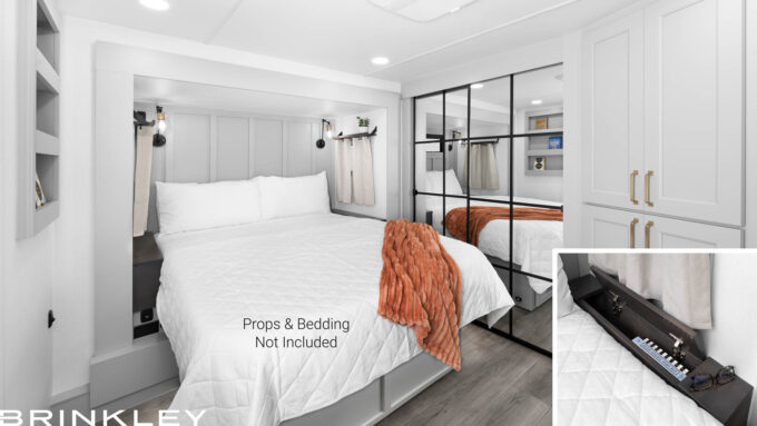 Interior of a Brinkley RV Model Gx 3500x bedroom featuring the optional queen-size bed flanked by two nightstands with built-in storage compartments, surrounded by windows.