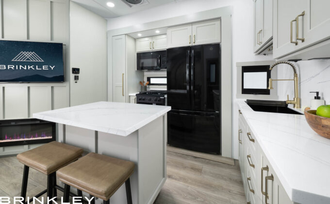 A spacious RV kitchen in the Brinkley Model Gx, showcasing hardwood trim, integrated LED lighting, and high-end residential-style hardware and finishes.