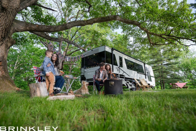Family Friendly Camping around a luxury Travel Trailer RV with kids playing with the family and dog around a campfire at their campsite